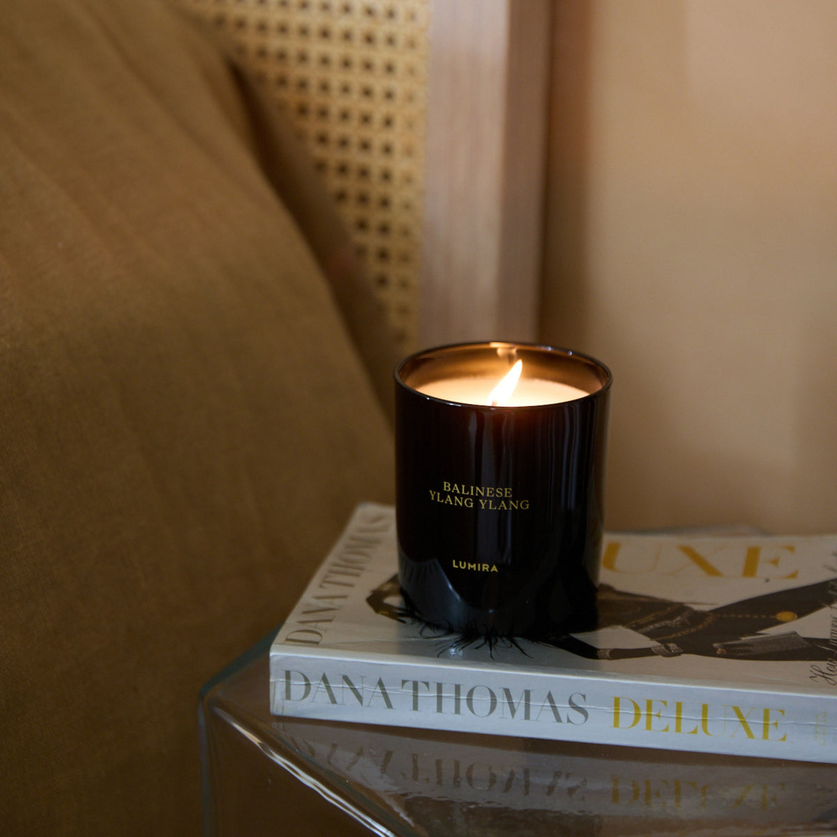 The LUMIRA Balinese Ylang Ylang candle lit on a stack of books beside the bed