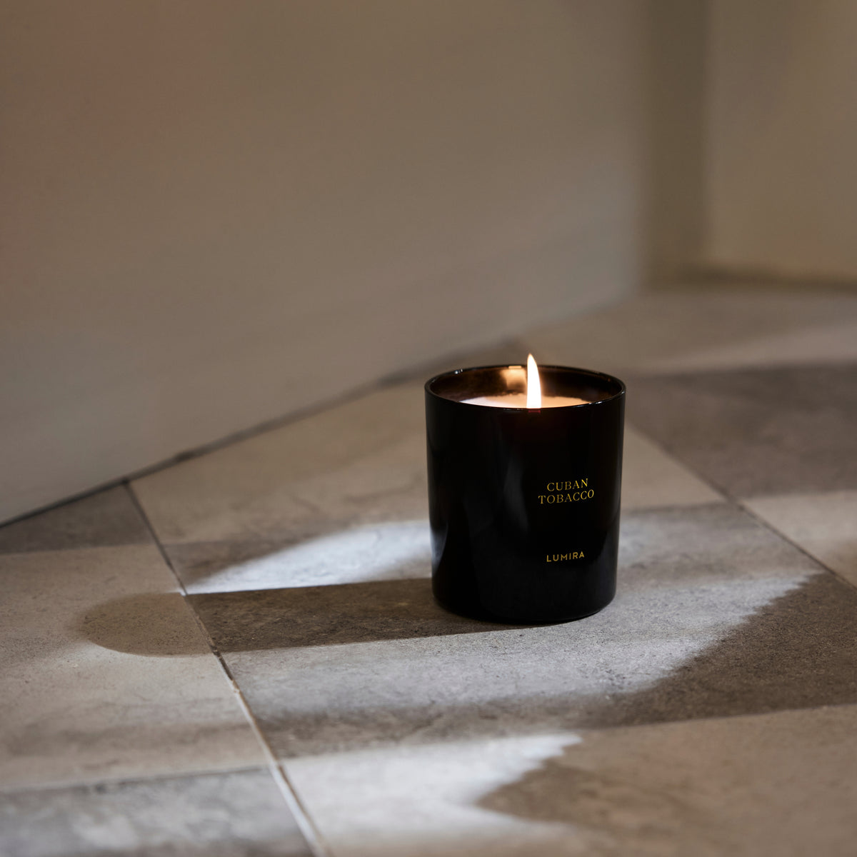 The LUMIRA Cuban Tobacco candle lit on a stone floor in afternoon sun