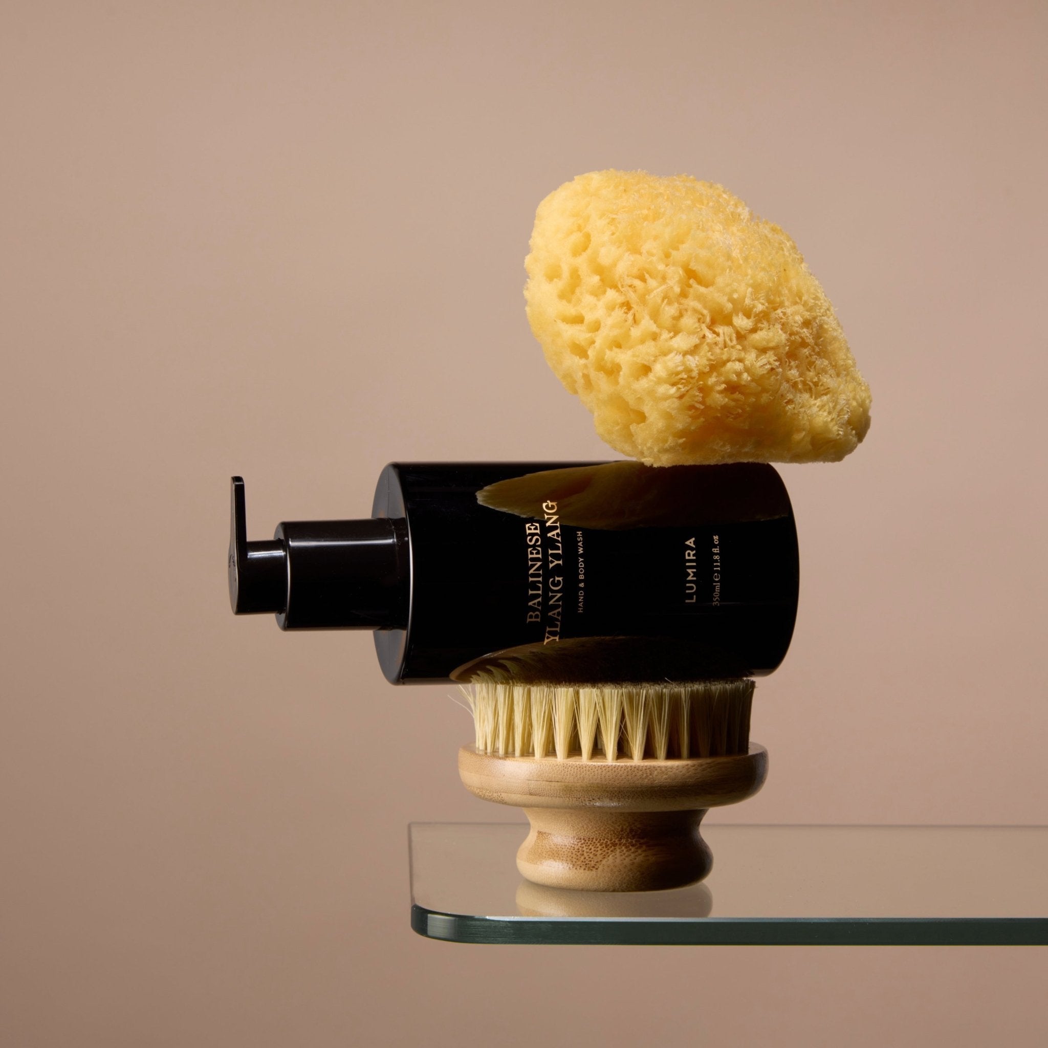 The LUMIRA Balinese Ylang Ylang Hand and Body Wash resting on a wooden body brush with a natural sea sponge on top